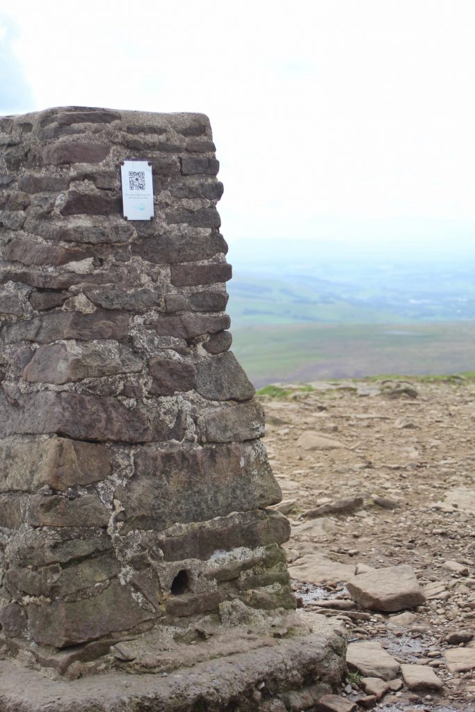 The Pen-y-Ghent trig point with a hazy view in the background