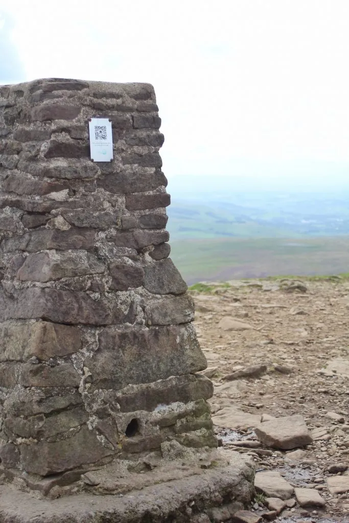 The Pen-y-Ghent trig point with a hazy view in the background