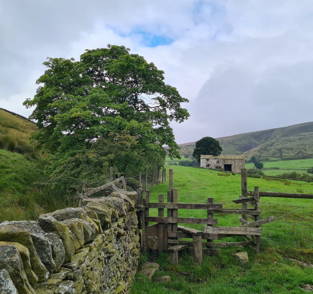 A wooden stile with a dilapidated barn and Pendle Hill in the background