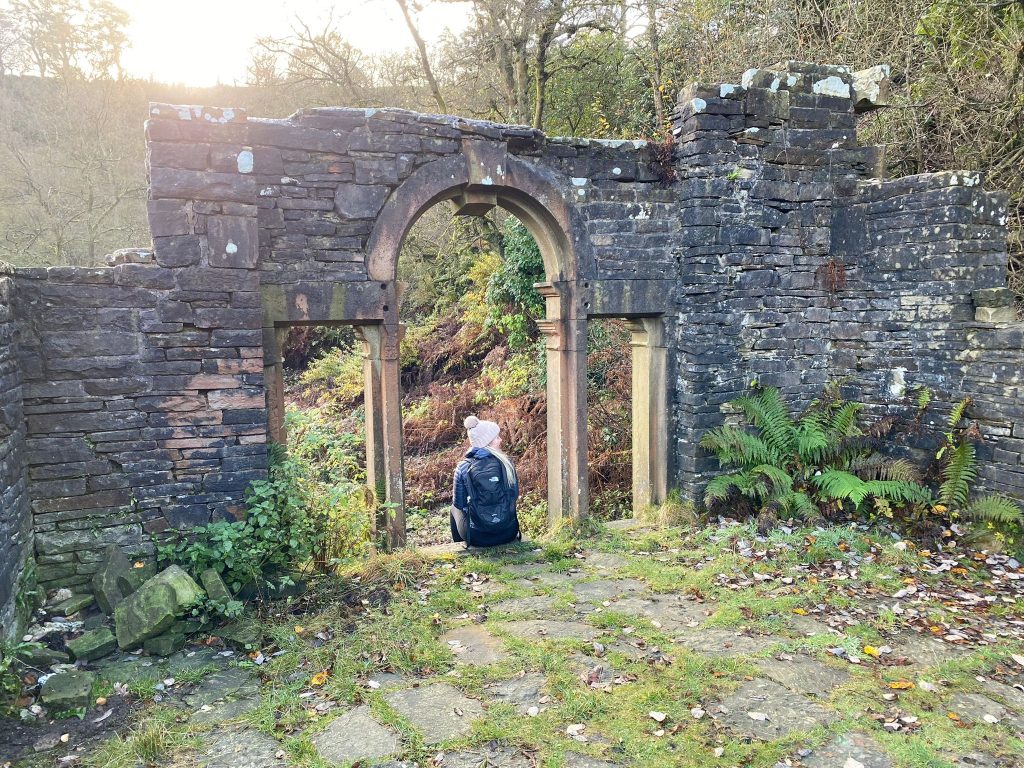 Blonde lady sitting in the ruins of Errwood Hall arched windows