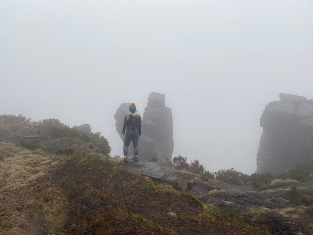 A woman standing in front of The Trinnacle above Dovestone Reservoir in the mist - The Wandering Wildflower