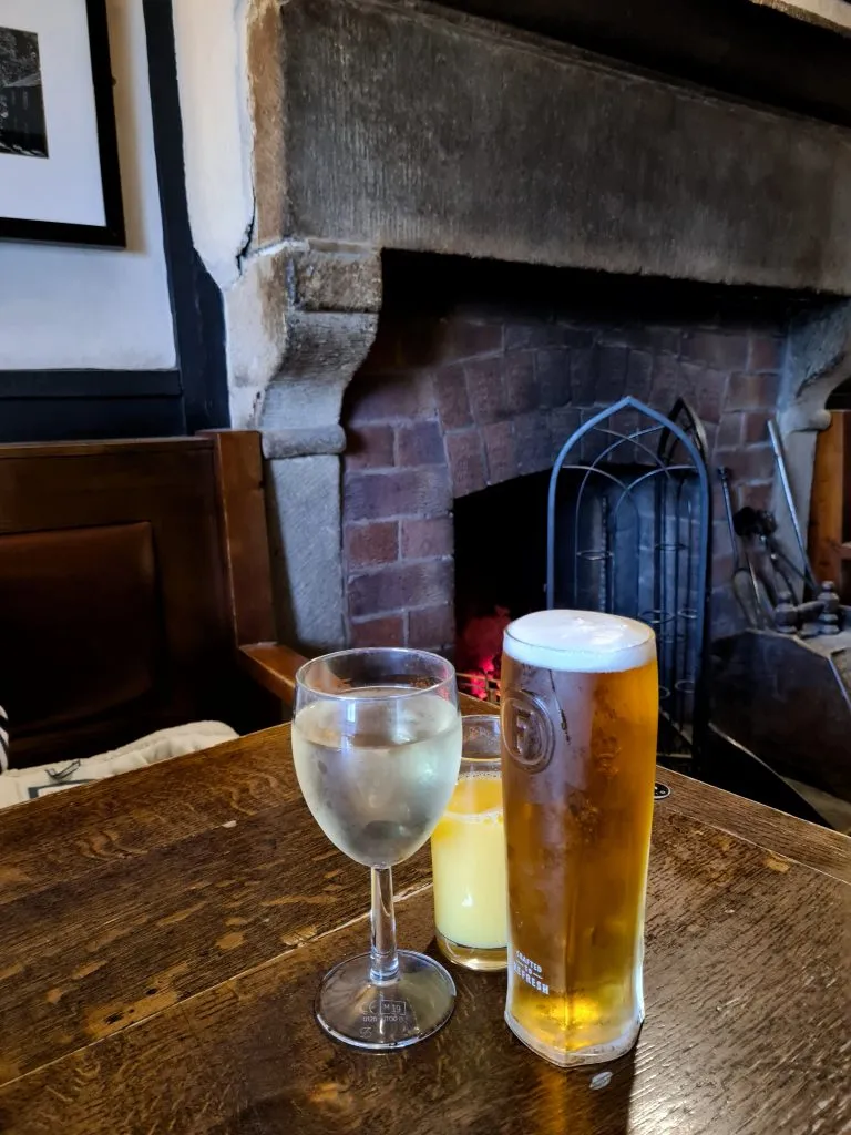 Glass of wine and a pint of lager in front of an open coal fire