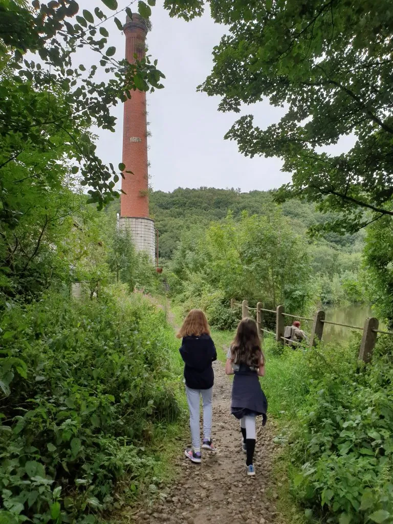 Two girls walking along a path towards an old brick mill chimney