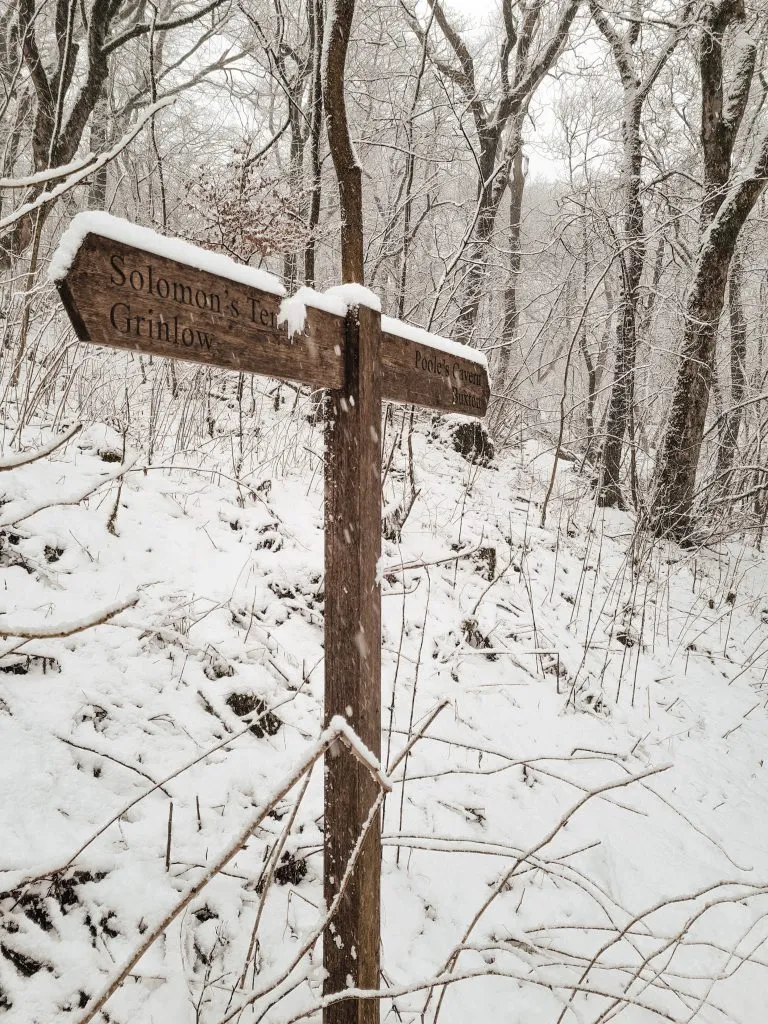 Wooden signpost in a woodland covered in snow, pointing the way to Solomon's Temple and Poole's Cavern