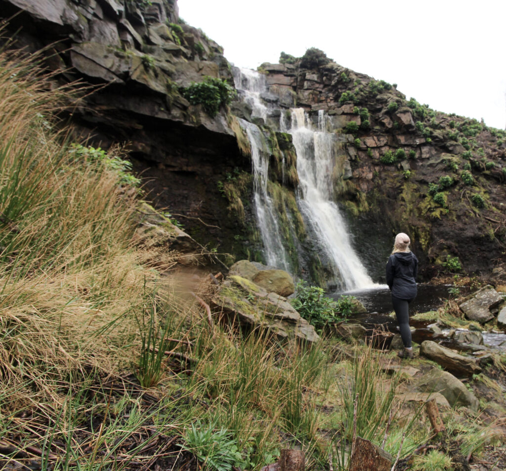 A woman stood at the bottom of a waterfall, looking up at the top