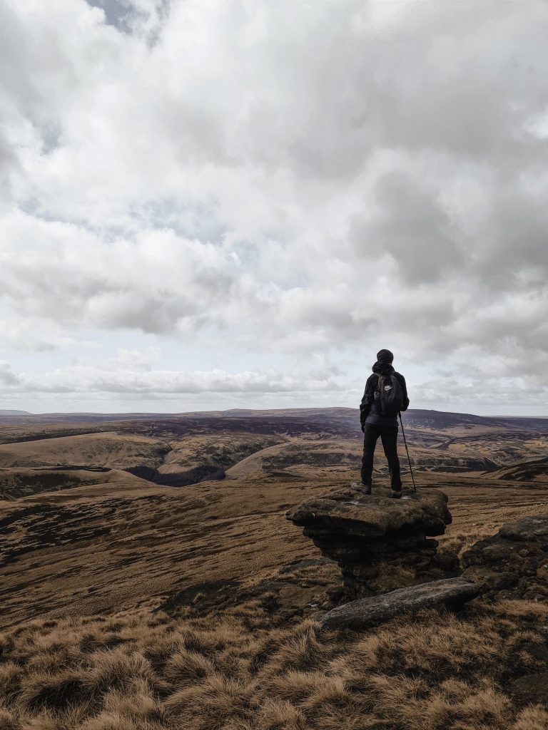 A man in dark clothes stands on a rock looking out over Howden Moors - Langsett to Margery Hill trig point walk by The Wandering Wildflower