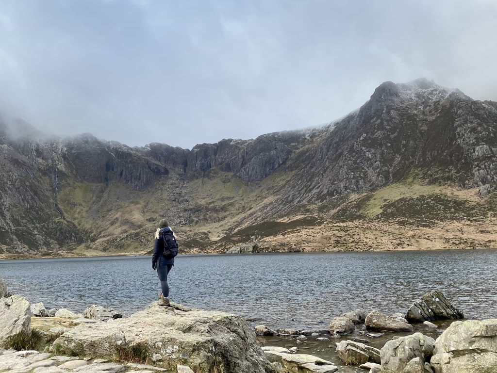 A woman standing on the shores of a lake Llyn Idwal looking up at Y Garn