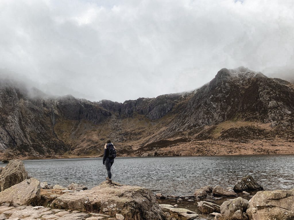 A woman standing on the shores of a lake Llyn Idwal looking up at Y Garn