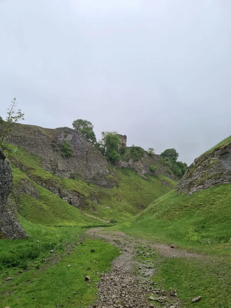 A steep sided valley with grassy sides and the ruins of a castle on the hillside