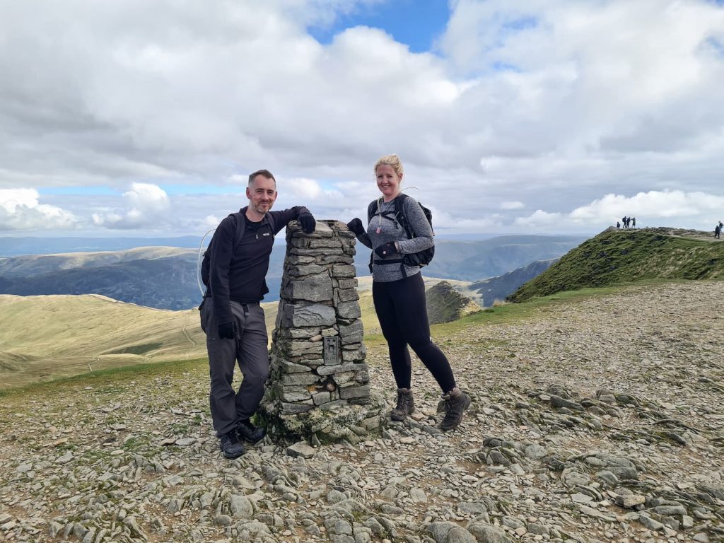 A couple posing with Helvellyn trig point - The Wandering Wildflower