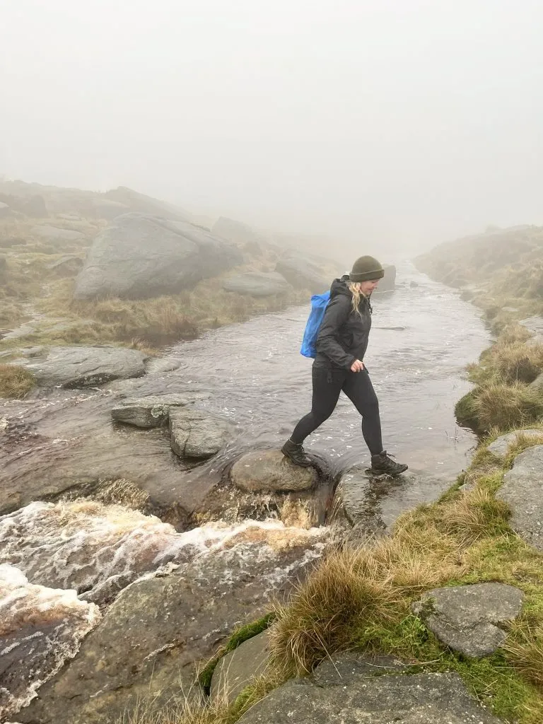 A woman crossing the River Kinder using stepping stones