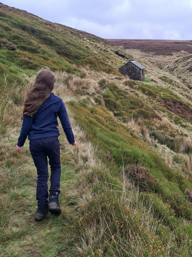 A small girl walking on the moors towards a cabin