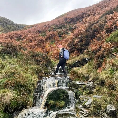 A woman crossing a waterfall at Blackden Brook