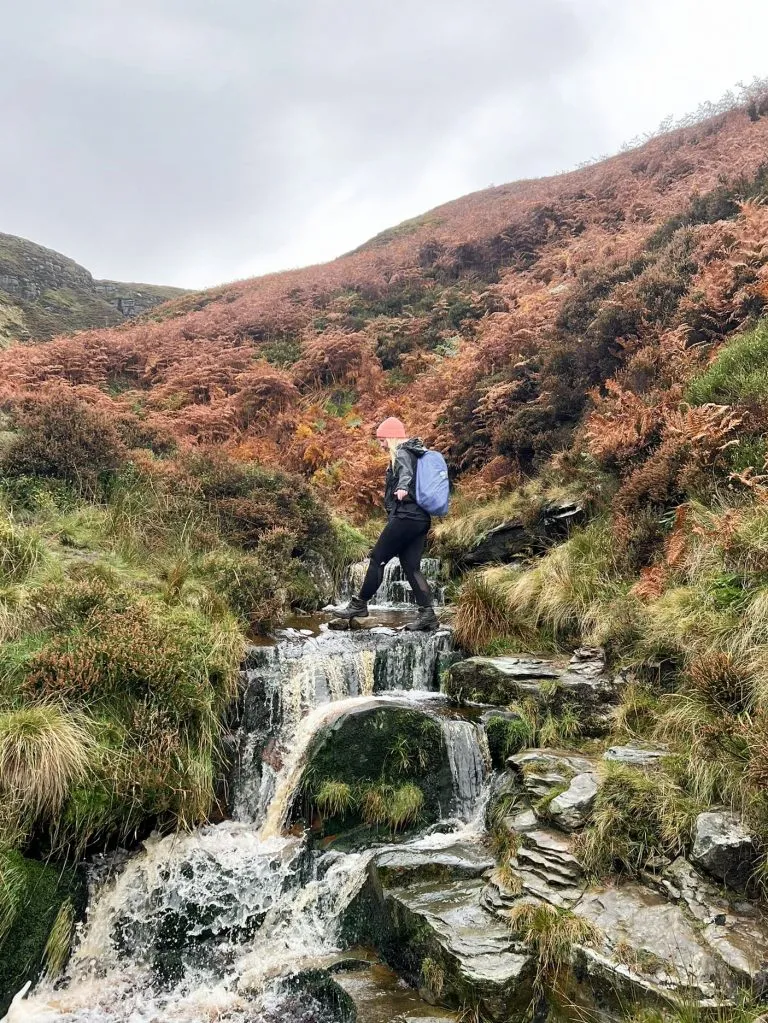 A woman crossing a waterfall at Blackden Brook