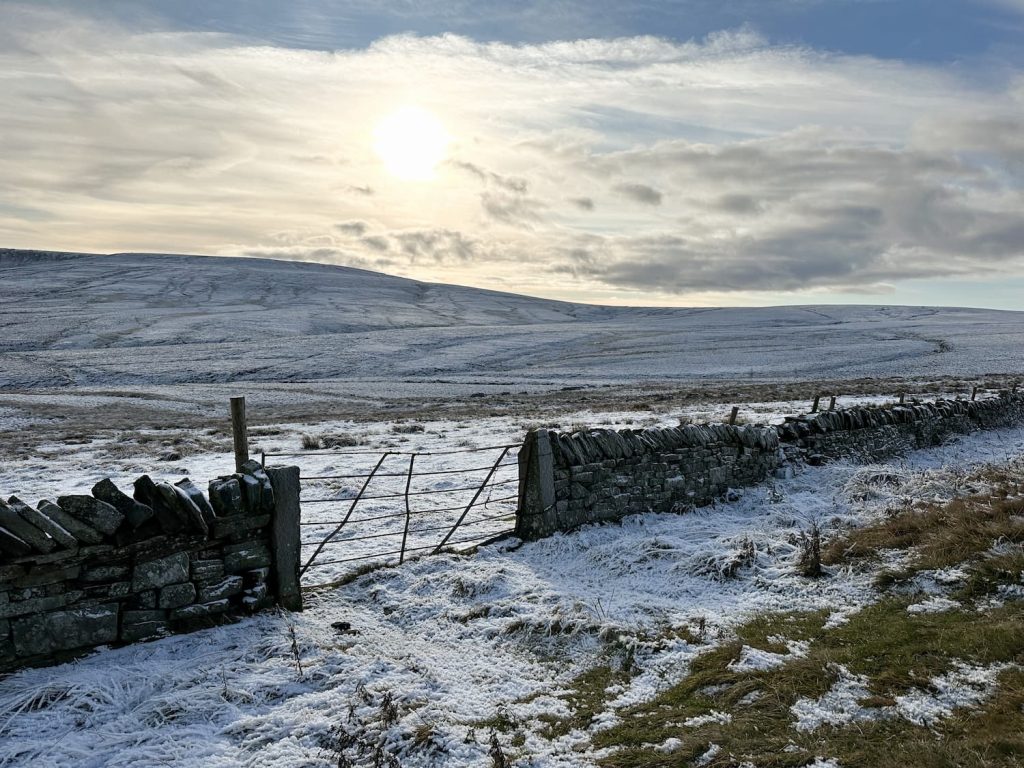 An iron gate with a view over snowy fields to Black Hill, Holmfirth