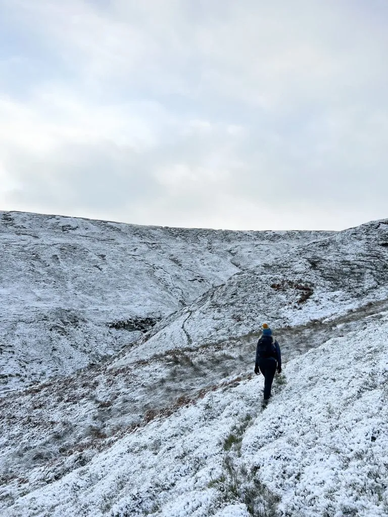 A woman walking on a snowy moor near Black Hill, Holmfirth