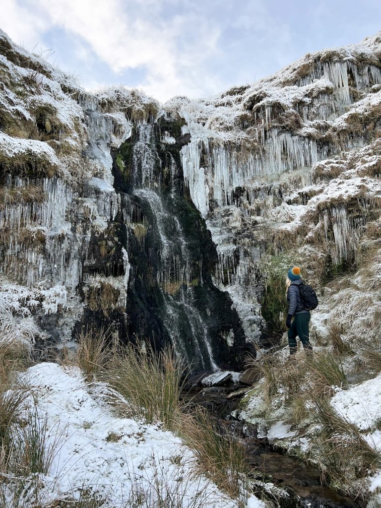 A woman standing looking at a frozen Issue Clough waterfall, Holmfirth