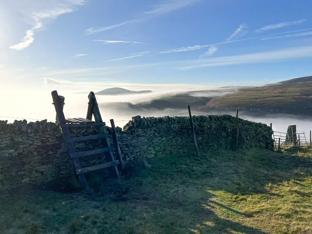 A stile in a stone wall with a cloud inversion in the Peak District