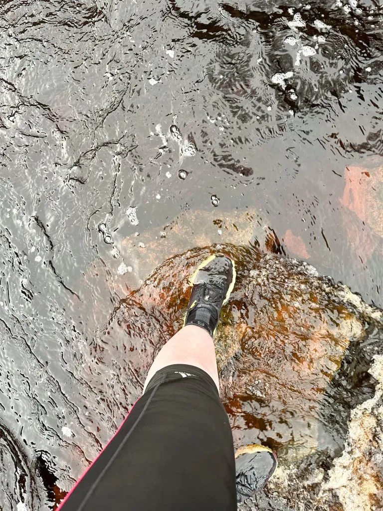 Someone crossing a river on stepping stones - the water level is higher than the trainers!