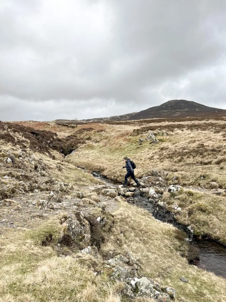 A woman crossing stepping stones near Bleaberry Fell