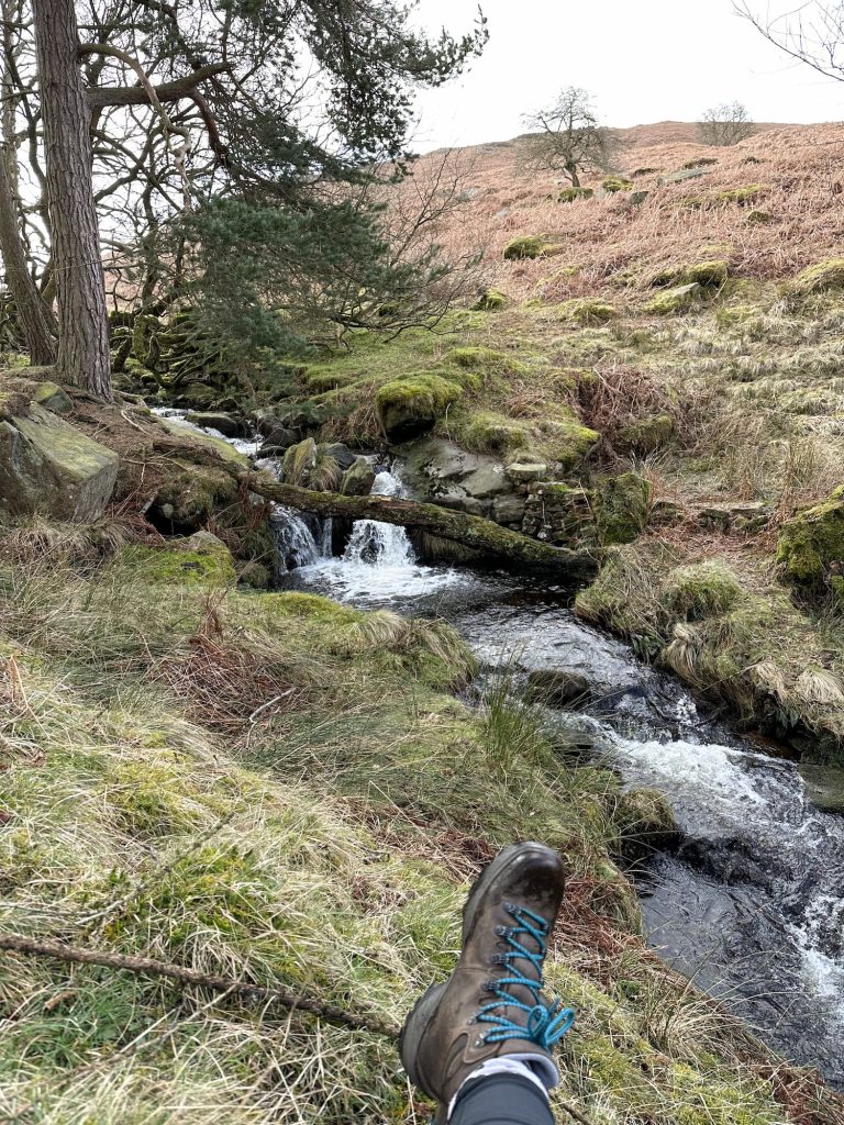 A view of a stream and waterfall with walking boots in the bottom of the frame