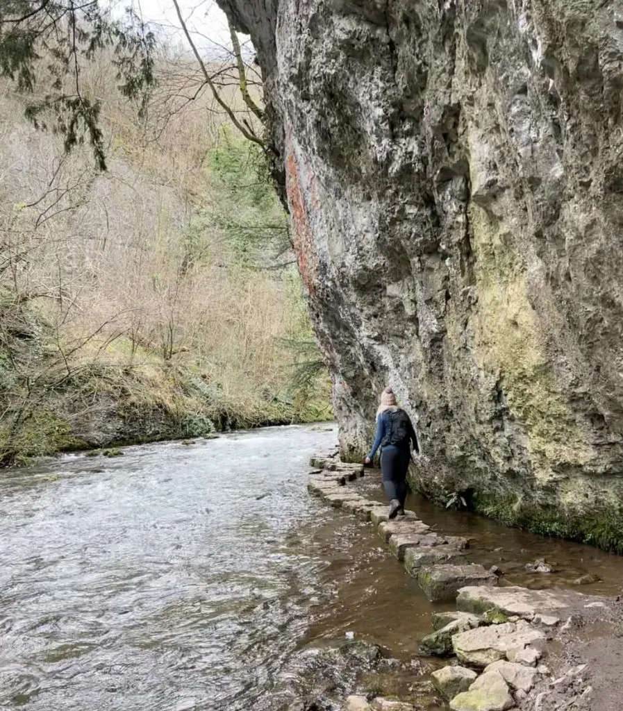 A woman walking over some stepping stones in Chee Dale