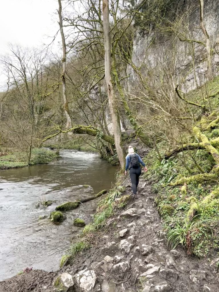 A woman walking on a rocky, uneven path next to a river