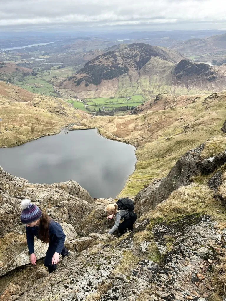 A young girl in a bobble hat and a woman climbing a mountain in the Lake District
