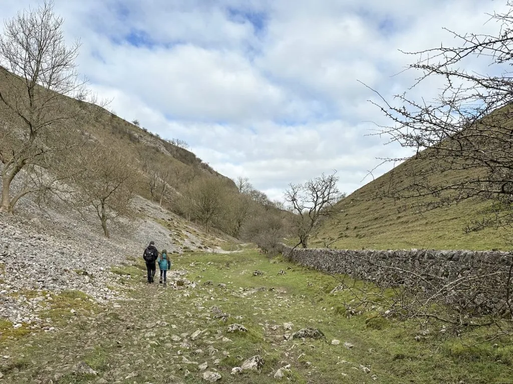 A father and daughter walking together through the steep limestone gorge of Biggin Dale