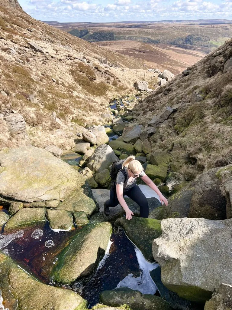 A blonde haired woman climbing up some rocks