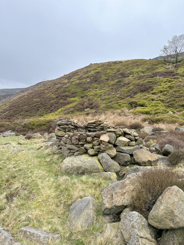 A rugged moorland view with a stone shelter in the valley bottom