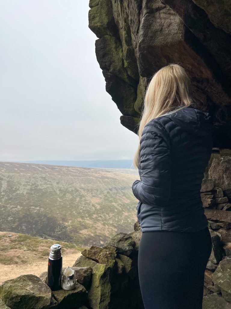 A woman looking out of a cave enjoying a flask of tea