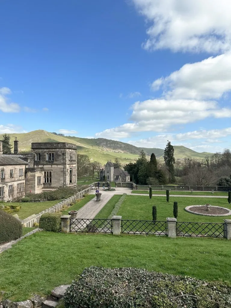 A grand house with formal gardens, with a view of Thorpe Cloud and Bunster Hill in the background