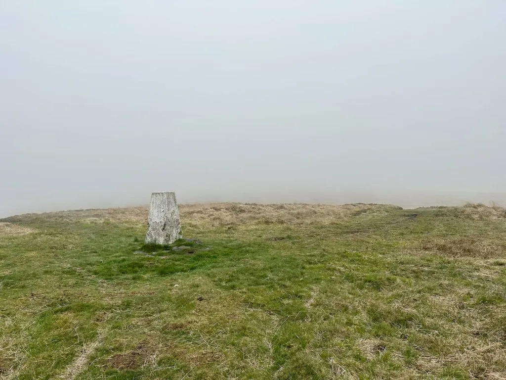 A misty view of Dog Hill trig point, a grey concrete pillar