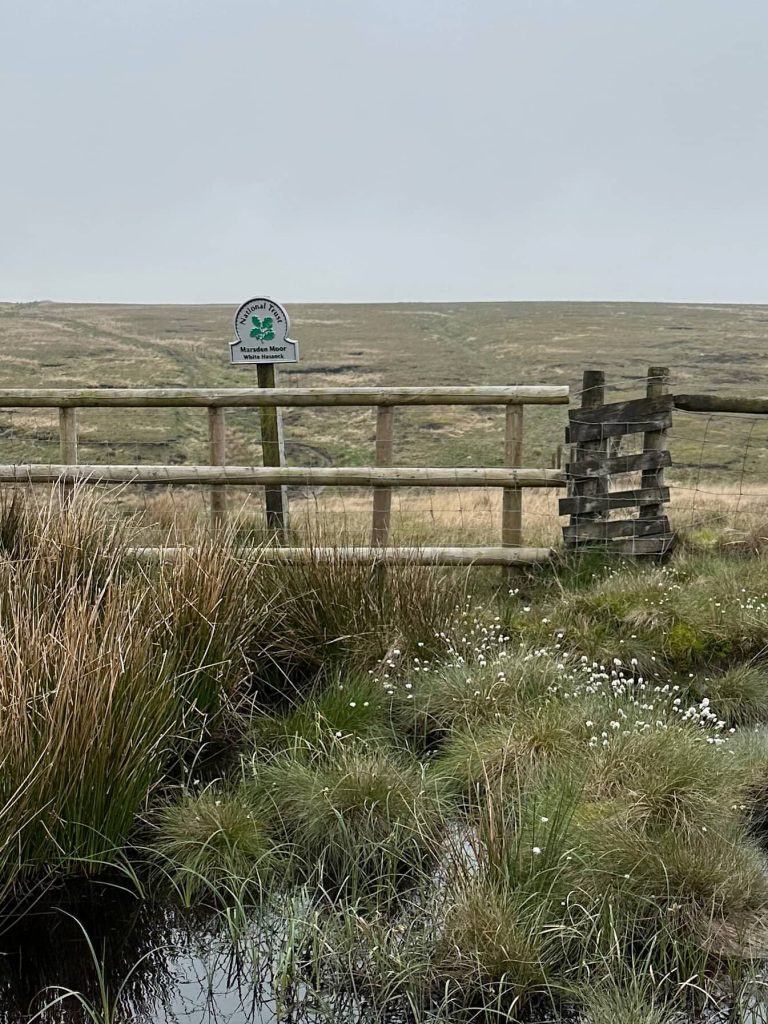 A fence on a boggy moorland with a National Trust Omega sign