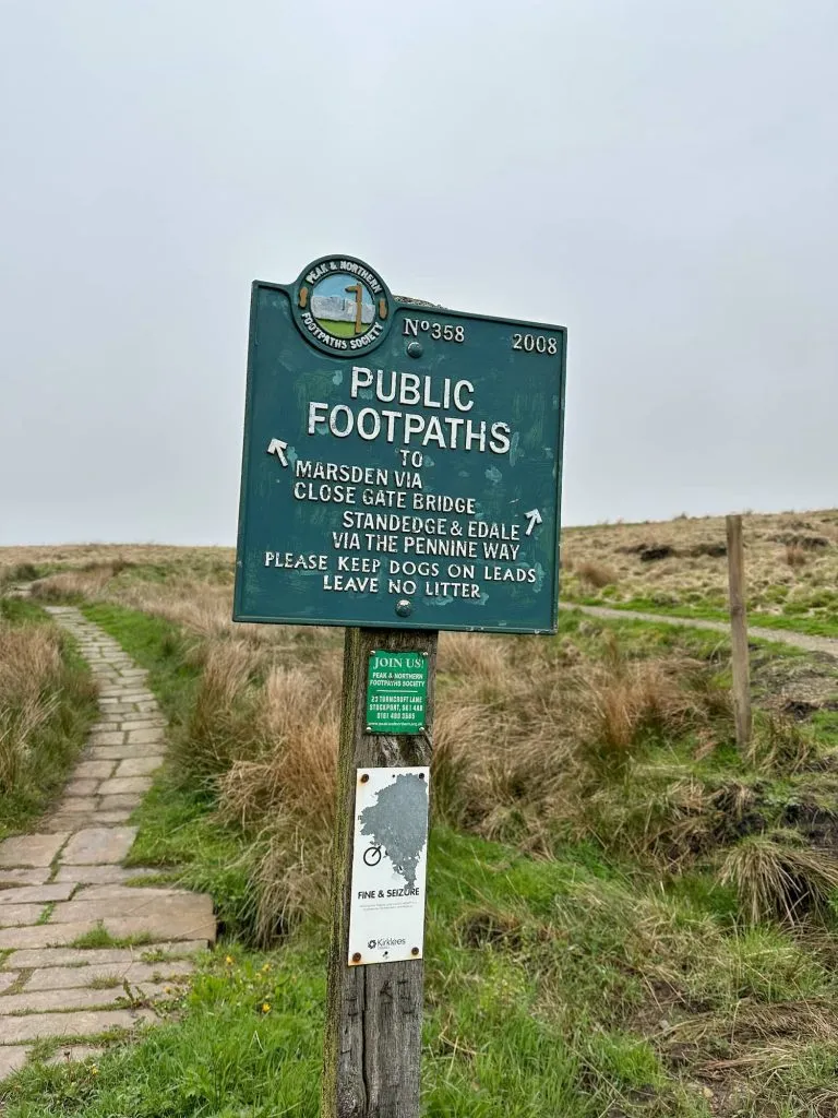 A green sign near a fork in the footpath