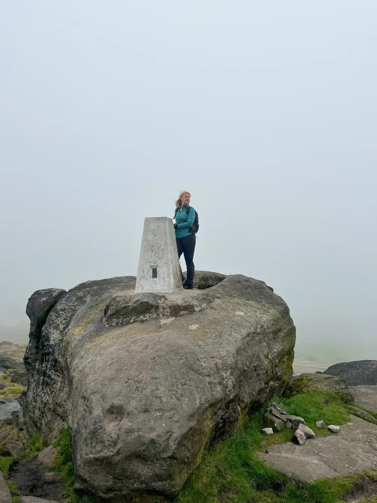 A woman standing next to the trig point at Blackstone Edge