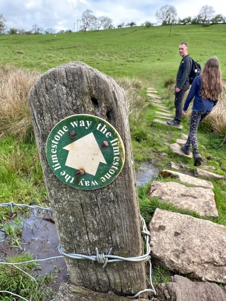 A wooden fence post with a way marker for the Limestone Way - green with white text and arrow