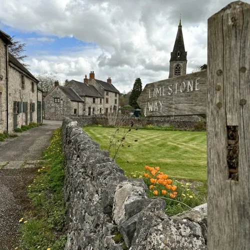 A wooden sign post for the Limestone Way pointing to a village scene, with some orange tulips