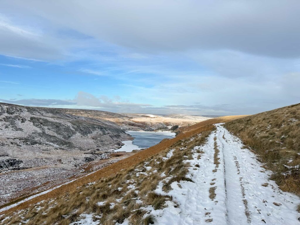 A snowy track running on a hillside high above a reservoir