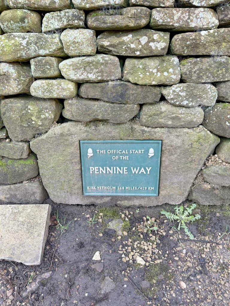A green plaque set into a wall marking the start of the Pennine Way