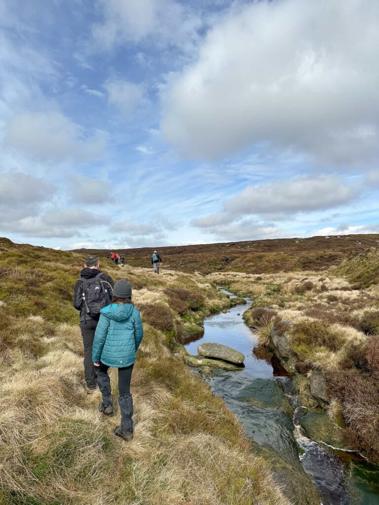 A father and daughter hiking on the moors next to a stream