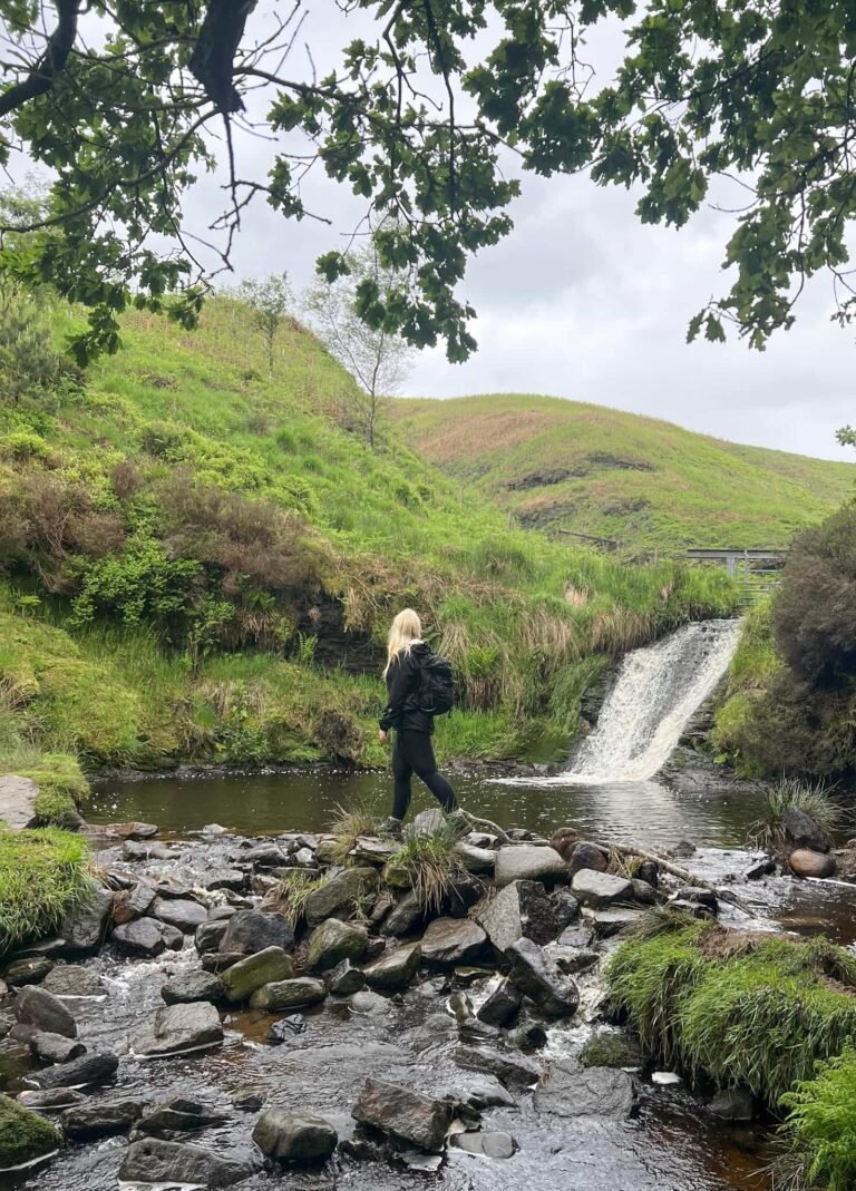 A woman walking on some stepping stones in front of a waterfall