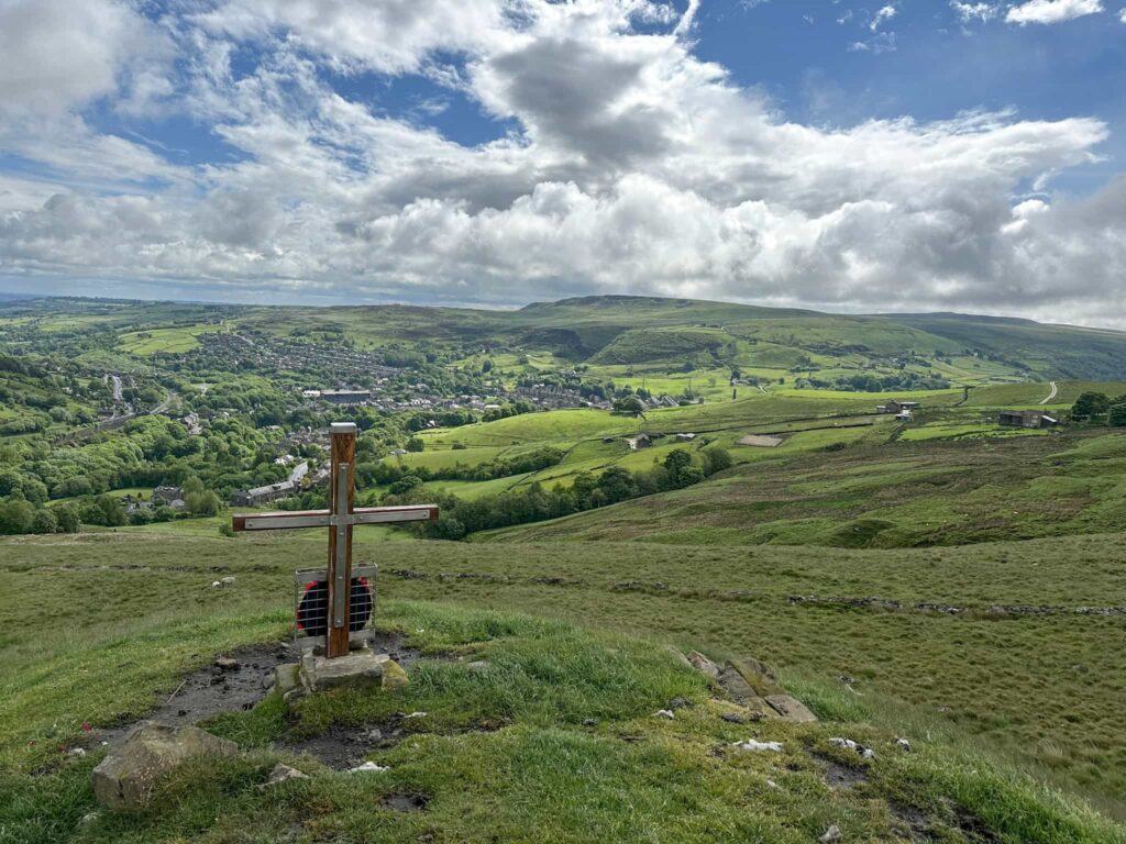 A wooden war memorial cross with views over the valley below