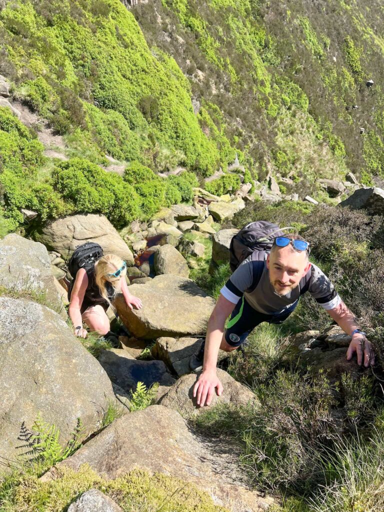 A couple climbing Blackden Brook, a rocky and grassy scramble in the Peak District