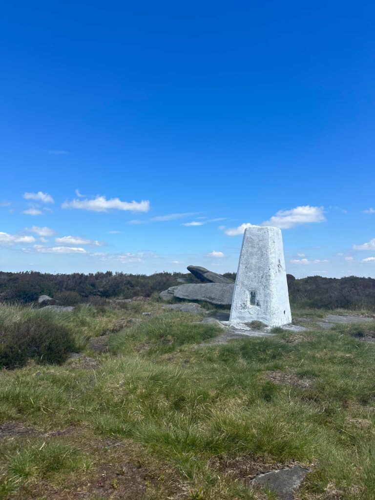 Margery Hill trig point, a white trig point surrounded by grass and a few gritstone boulders