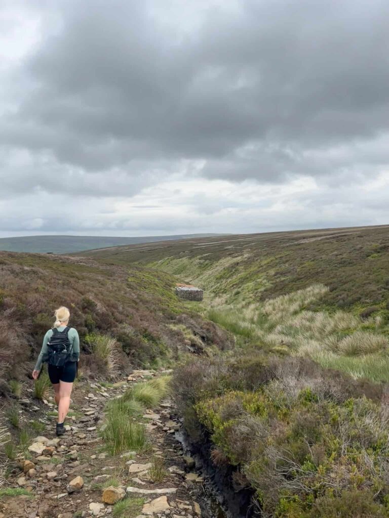 A woman walking down a gamekeepers track towards a small cabin