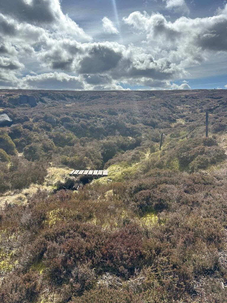 A small wooden bridge crossing Stable Clough, a moorland stream