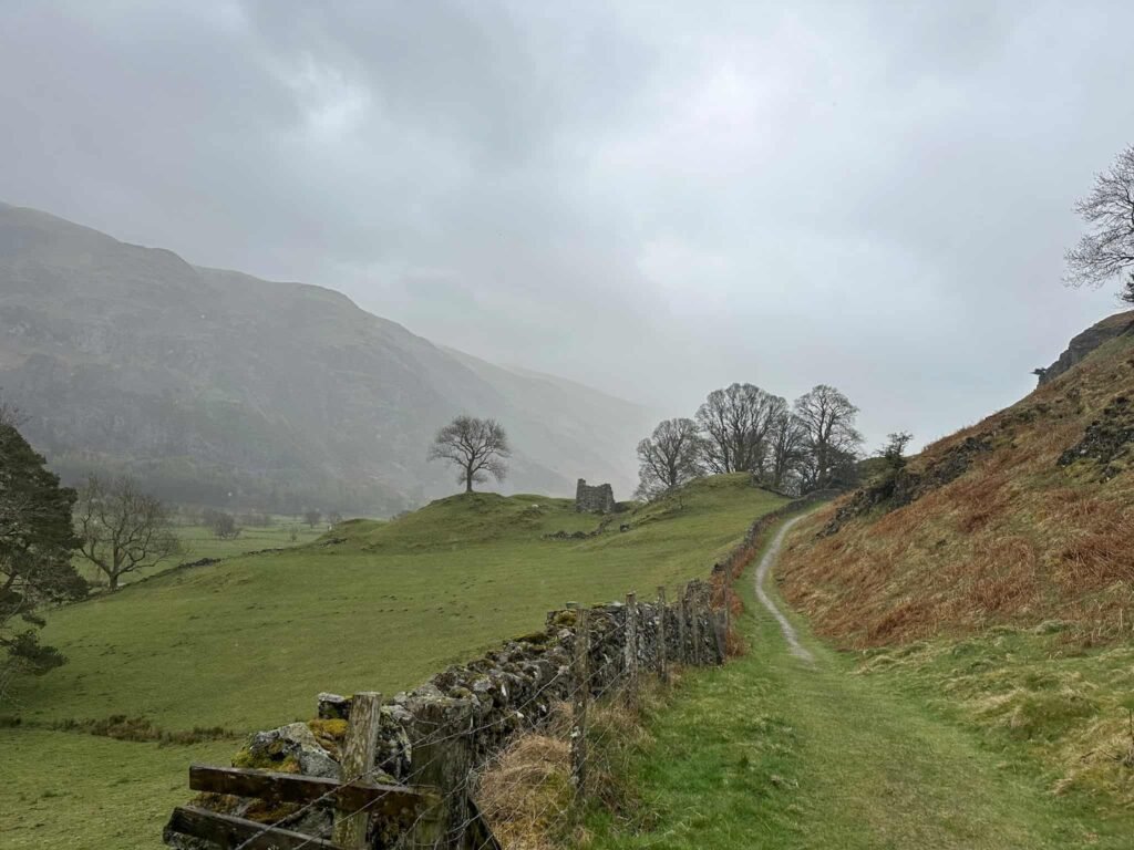 A misty murky view of a ruined farm building with the Helvellyn massif in the background