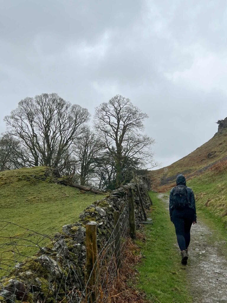 A woman walking on a path, next to a stone wall, in the rain